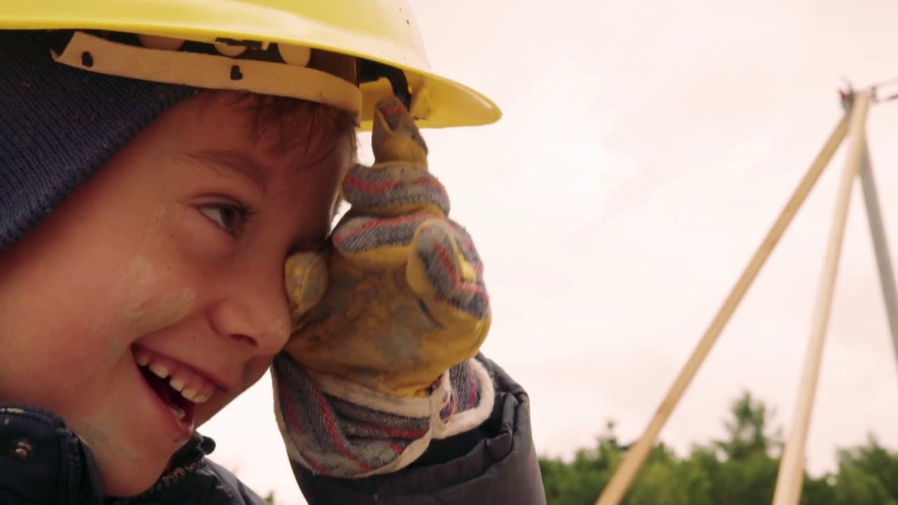 Kind mit gelbem Bauhelm und Arbeitshandschuhen auf der Baustelle